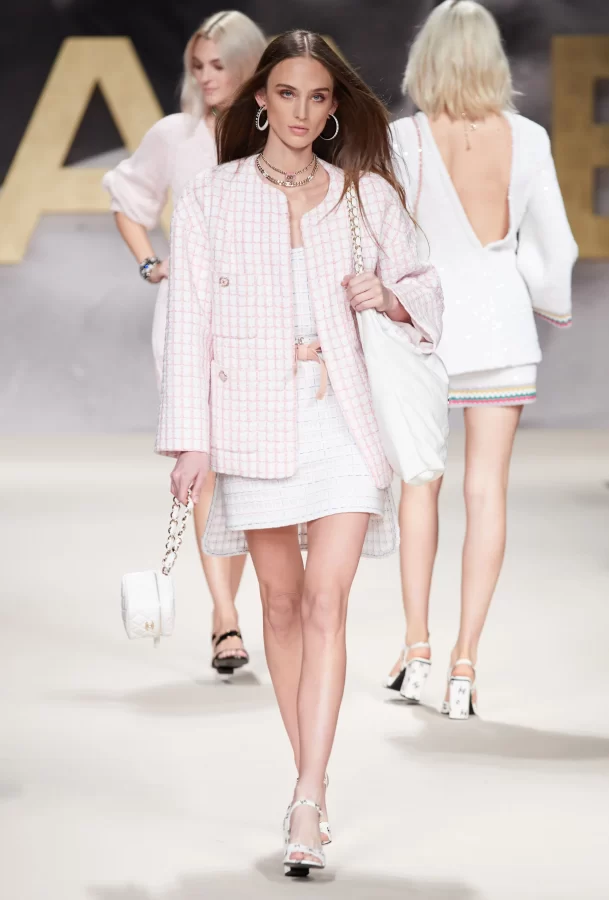 A 90s Chanel callback in the SS22 Chanel show, model wears a white tweed dress with a pastel pink classic Chanel jacket.