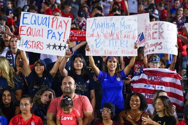 Women holding signs at one of the U.S. womens national soccer teams games that   display their dedication towards equal gender pay. 